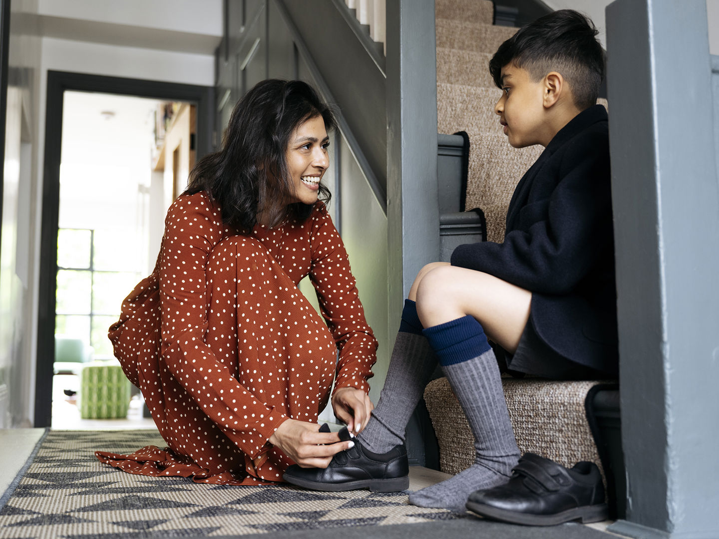 Child sitting on stairs while mother ties his shoes